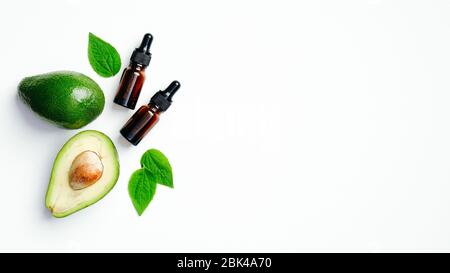 Avocat mûr frais avec bouteilles d'huile essentielles et feuilles vertes sur fond blanc. Cuisine saine ou concept de cosmétiques biologiques naturels spa. Pose plate Banque D'Images