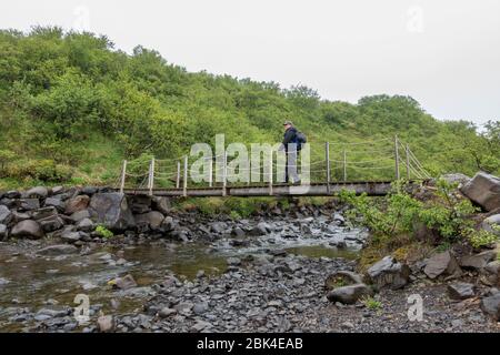 Un homme qui marche à travers un petit pont près de Skaftafell, parc national de Vatnajökull, sud de l'Islande. Banque D'Images