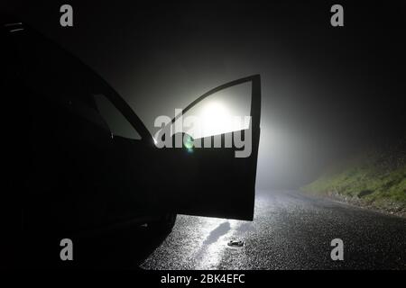 Une voiture garée, avec porte ouverte, sur le côté de la route, sous un feu de rue. Une nuit d'hiver brumeuse Banque D'Images