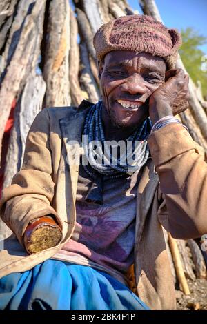 Portrait d'un homme d'une main Himba assis dans une vieille chaise à l'extérieur de sa cabane. Banque D'Images