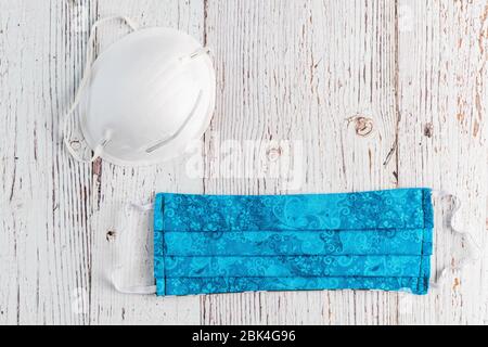 Masque de protection en tissu bleu fait main, et masque commercial blanc, sur fond blanc rustique Banque D'Images