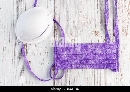 Masque de protection en tissu violet fait main, et masque commercial blanc, sur fond blanc rustique Banque D'Images