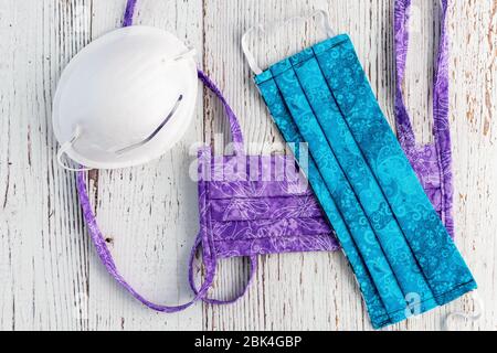 Masques de protection faits main en tissu bleu et violet, masque commercial blanc, sur fond blanc rustique Banque D'Images