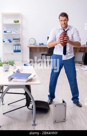 Jeune employé jetant du ballon de rugby dans le bureau Banque D'Images