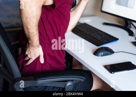 Homme souffrant de douleurs dorsales tout en travaillant à domicile dans un bureau improvisé dans le salon Banque D'Images