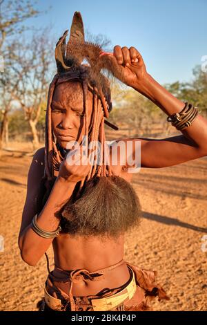 Batwa fille dans la robe traditionnelle combater ses cheveux au coucher du soleil. Banque D'Images