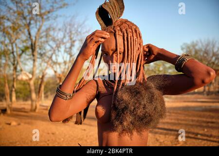 Batwa fille dans la robe traditionnelle combater ses cheveux au coucher du soleil. Banque D'Images