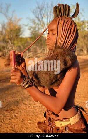 Batwa fille dans la robe traditionnelle combater ses cheveux au coucher du soleil. Banque D'Images