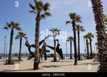 Vue sur la plage de Barceloneta, la plage la plus populaire de Barcelone, Catalogne, Espagne. La sculpture olympique parmi les palmiers vus au loin. Banque D'Images