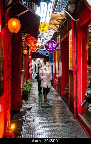 Une jeune femme chinoise marche dans une ruelle à Tianzifang par temps humide. Shanghai, Chine. Banque D'Images