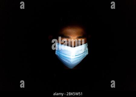 Un jeune homme bleu portant un masque chirurgical jouait à Dhaka pour jouer à des jeux sur smartphone. Banque D'Images