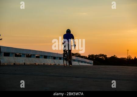 Silhouette d'un homme fait du vélo au coucher du soleil.fond bleu-orange. Banque D'Images