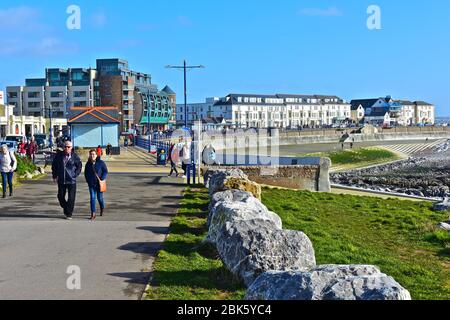 Une vue lointaine sur les bâtiments de bord de mer bordant l'esplanade à Porthcawl.zone de 'plage' artificielle à marée basse.les gens appréciant la marche au bord de la mer. Banque D'Images