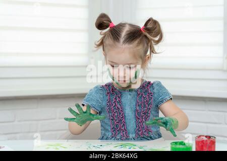 Petite fille peint avec les doigts.petite fille souriant, abaisse ses paumes dans la peinture pour faire une empreinte, auto-isolation, coronavirus covid-19, rester à la maison Banque D'Images