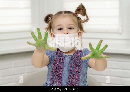 Petite fille dans les peintures de masque avec les doigts.girl nous montre ses palmiers verts dans la peinture, auto-isolation, coronavirus covid-19, rester à la maison Banque D'Images