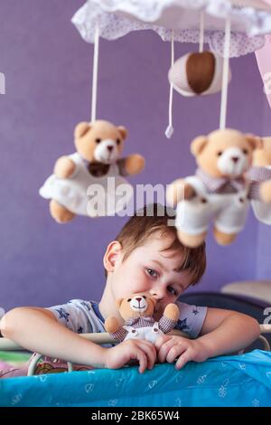 Adorable petit garçon debout près d'un lit bébé avec carrousel mobile de musique de bébé. Big Brother regarde la jeune sœur dans le lit de bébé Banque D'Images