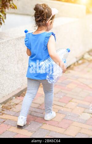 Vue arrière petite fille tenant des bouteilles d'eau en plastique pour recyclage. Enfant sortant des ordures recyclables séparées. Concept de monde sans plastique, zéro déchet. Banque D'Images