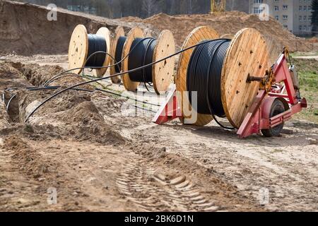 Plusieurs bobines de bois avec câble d'alimentation posé dans une tranchée. Concept de fourniture d'électricité pour les projets de construction. Banque D'Images
