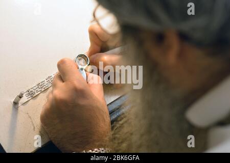 Un rabbin orthodoxe et un scribe corrigent le lettrage hébreu sur le parchemin à utiliser à l'intérieur d'une mezzuzah. À Crown Heights, Brooklyn, New York. Banque D'Images