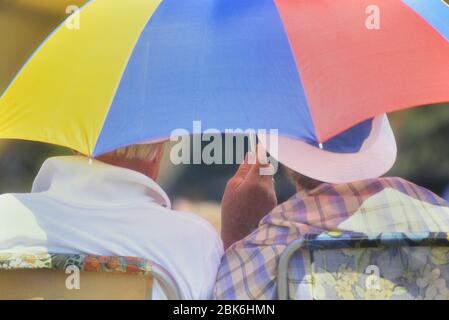 Couple âgé assis sous un parapluie offrant une protection contre la chaleur et le soleil, Angleterre, Grande-Bretagne, Royaume-Uni Banque D'Images