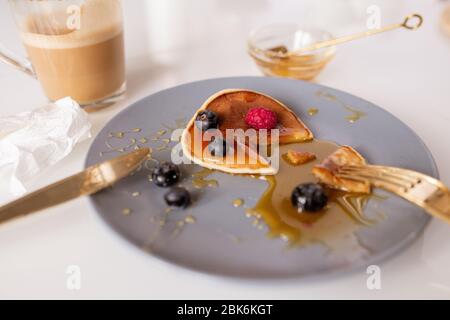 Petite crêpe maison avec miel, framboises et mûres mangés par quelqu'un pour le petit déjeuner à la table le matin Banque D'Images