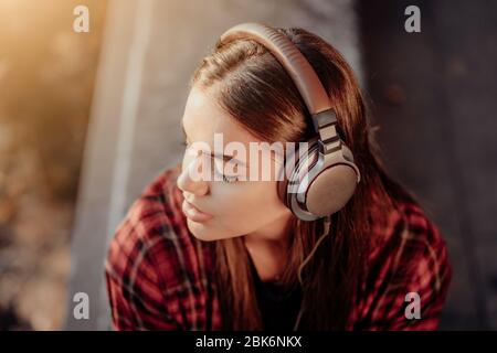 Un adolescent écoute de la musique par des écouteurs dans Park.Girl in rouge plaid shirt sourires, dansant sur rythme.concept de vie étudiant, liberté, moderne Banque D'Images