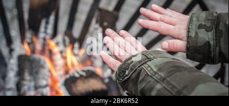 Vue de dessus détaillée de la femme chauffant ses mains autour de la flamme chaude dans la cheminée à froid hiver saison. Rue urbaine extérieure Banque D'Images