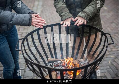 Vue de dessus détaillée de la femme chauffant ses mains autour de la flamme chaude dans la cheminée à froid hiver saison. Rue urbaine extérieure Banque D'Images