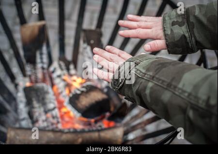 Vue de dessus détaillée de la femme chauffant ses mains autour de la flamme chaude dans la cheminée à froid hiver saison. Rue urbaine extérieure Banque D'Images