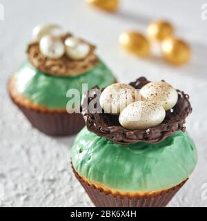 Délicieux cupcakes décorés de glaçage avec un nid et des œufs de chocolat, gros plan. Banque D'Images