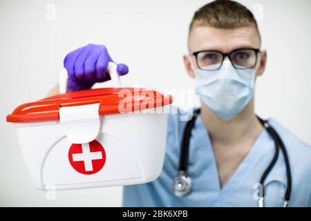 paramedic dans le masque, les lunettes et les gants en latex bleu contient un boîtier médical croisé rouge Banque D'Images