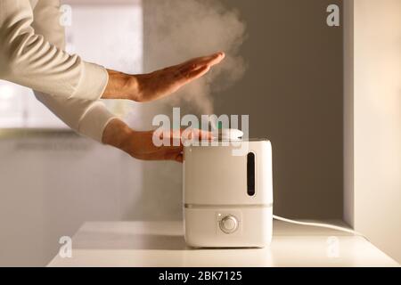 Homme tenant main sur vapeur diffuseur d'huile d'arôme sur la table à la maison, vapeur de l'humidificateur d'air. Technologie ultrasonique, augmentation de l'humidité de l'air dans Banque D'Images