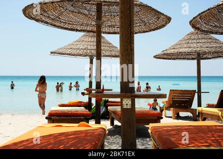 Les gens qui apprécient ensemble dans l'eau de mer turquoise colorée, le soleil de la journée, dans la belle plage. Parasols en paille et chaises longues en bois sur une plage tropicale n Banque D'Images
