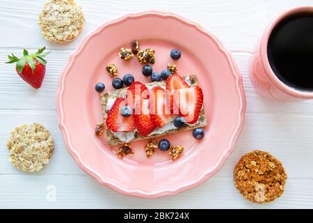 Petit déjeuner sain et savoureux, sandwich aux fruits avec fraise et myrtille, biscuits aux céréales naturels sur table blanche, vue sur le dessus. Banque D'Images