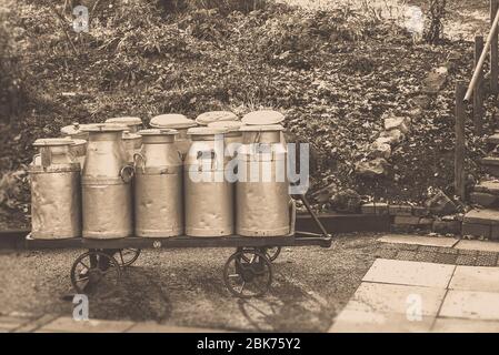 Sepia, churns de lait d'époque en trolley à la gare du patrimoine, Severn Valley Railway, Royaume-Uni. Production et distribution de lait britannique. Lait Royaume-Uni. Banque D'Images