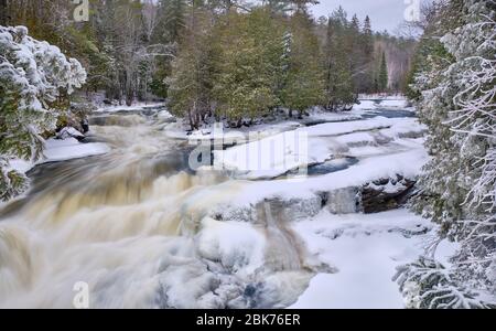 En hiver, après une chute de neige fraîche, l'eau de rouage de la chute d'Egan chutes près de Bancroft, s'étend entre la rive bordée d'arbres rocheux enneigés. Banque D'Images