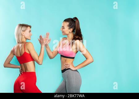 Super entraînement. Deux jeunes filles sportives et heureux dans les vêtements de sport se donnant cinq autres haut tout en se tenant contre fond bleu Banque D'Images