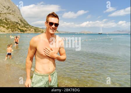 Homme souriant dans les lunettes de soleil bronzer au bord de la mer Banque D'Images