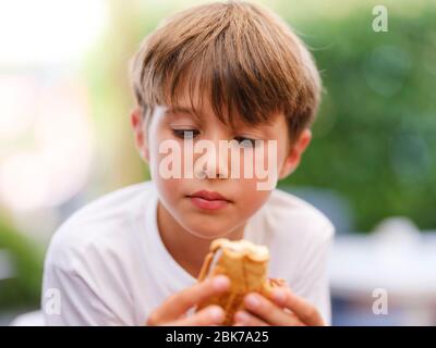 Gros plan portrait de beau, mignon, petit garçon, tenant le sandwich de glace dans sa main, regardant la glace Banque D'Images