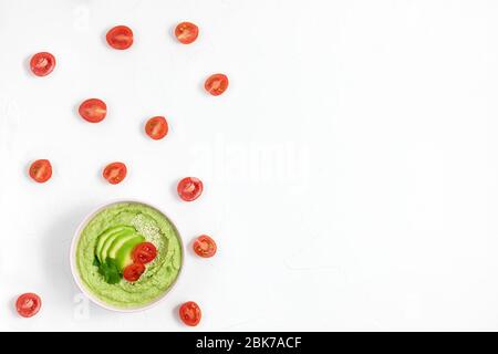 houmous composé d'avocats et de pois verts, de pois chiches dans des bols. sur fond blanc décoré de tomates. espace de copie. plat Banque D'Images