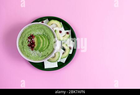 houmous composé d'avocats et de pois verts, de pois chiches dans des bols. sur un fond rose, avec des chips de pain. espace de copie. plat Banque D'Images