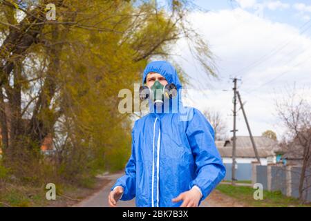 homme en combinaison bleue protectrice et respirateur masqué debout dans la rue, mesure de sécurité de quarantaine, éclosion de pandémie covid-19. Banque D'Images