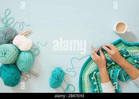 Les mains des femmes sont grandes. Femme croquettes. Fils de couleurs vert, turquoise, bleu et bleu. Fond en bois bleu. Banque D'Images