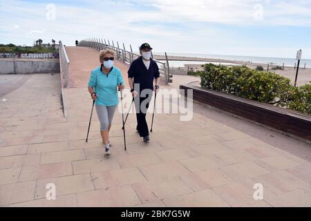 Un couple porte des masques de visage par mesure de précaution contre le covid 19 tout en marchant avec des bâtons de marche nordique dans une rue le long de la plage.l'Espagne lève certaines des restrictions d'état d'alarme dans lesquelles les gens peuvent aller faire des sports individuels entre 6 h et 10 h et entre 8 h. pm et 23 h la nuit. Les personnes à charge qui doivent sortir accompagnés sont réservées un horaire de 10 h à 12 h et de 19 h à 20 h. Banque D'Images