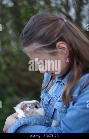 Portrait d'une jeune fille blonde tenant doucement un lapin animal de compagnie, lapin dans ses bras dehors dans le jardin. Banque D'Images