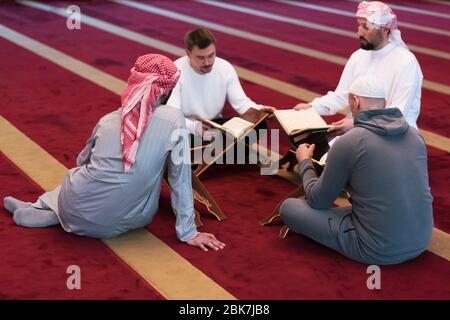 Groupe de jeunes musulmans religieux muliéthniques priant et lisant ensemble Koran à l'intérieur de la belle mosquée moderne. Banque D'Images