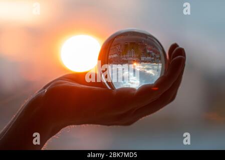 Soleil et boule de verre en main, homme tenant boule de cristal, lentille de cristal avec rayons de soleil et ville comme réflexion Banque D'Images