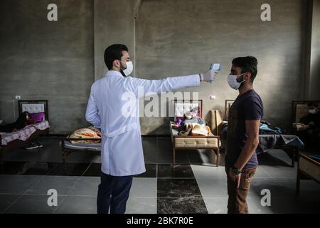 Jisr Al Shughur, Syrie. 02 mai 2020. Un medic contrôle la température d'un homme à l'intérieur d'un centre d'isolement sanitaire qui a été établi aux frontières syro-turque afin de placer les personnes venant de Turquie à Idlib comme mesure préventive contre la propagation de la maladie du coronavirus (COVID-19). Le centre est supervisé par une équipe médicale formée à toutes les mesures à prendre pour traiter les expatriés puisque le centre a reçu plus de 600 personnes jusqu'à présent et la période d'isolement est de 15 jours. Crédit: Anas Alkharboutli/dpa/Alay Live News Banque D'Images