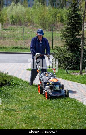 Ukraine, Kiev - 1er mai 2020: Travailleur de rue. Un homme au visage méconnaissable tond la pelouse avec une tondeuse. Faucher de l'herbe sur la pelouse. Banque D'Images