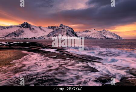 Vue sur Ersfjord depuis les rochers colorés au coucher du soleil et les rockpools jusqu'aux montagnes enneigées lors d'une journée sombre et nuageux, Cape Tungeneset, Senja, Norvège. Europe. Long e Banque D'Images